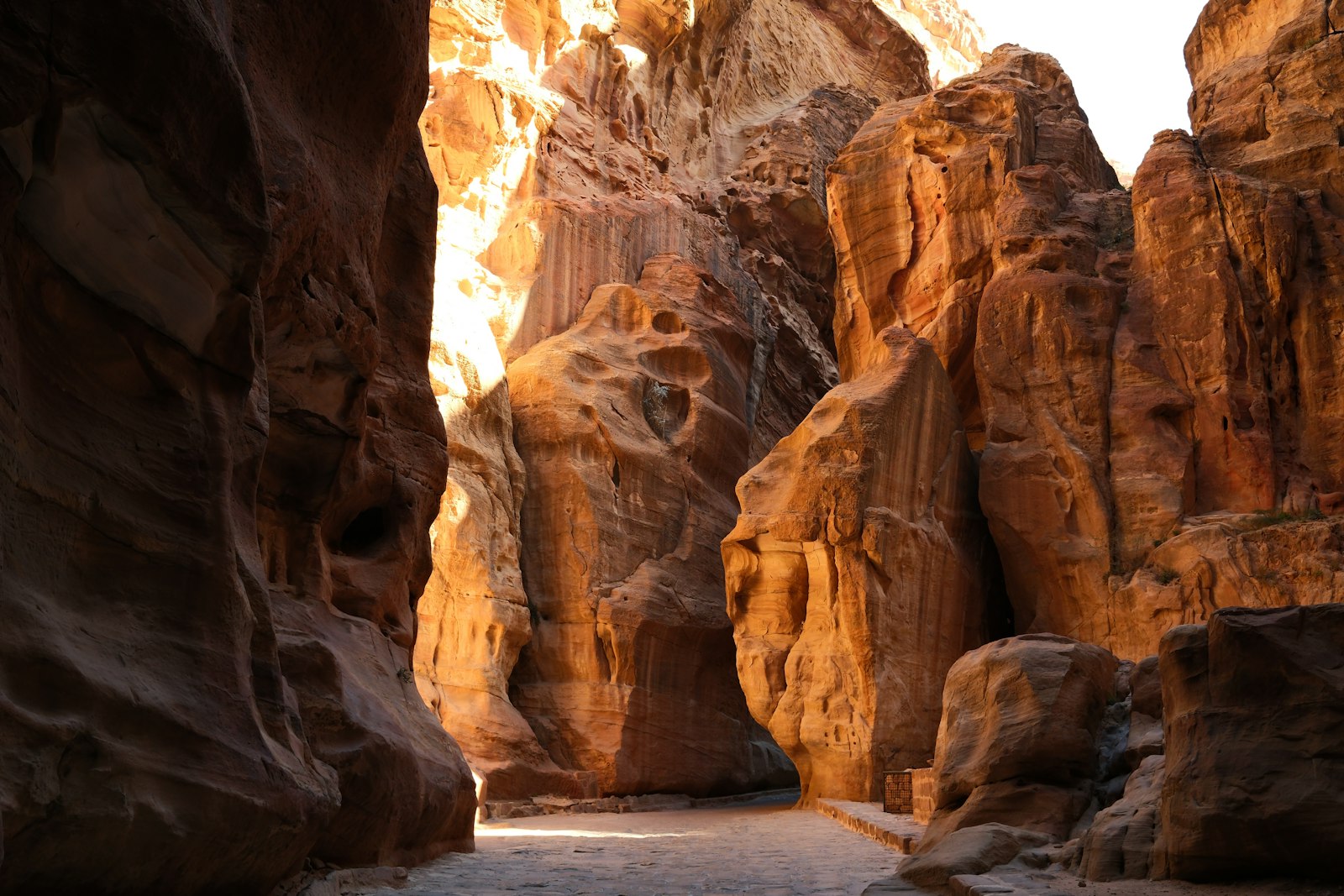 Sunlit sandstone canyon walls of the Siq winding toward Petra's Treasury in warm golden light